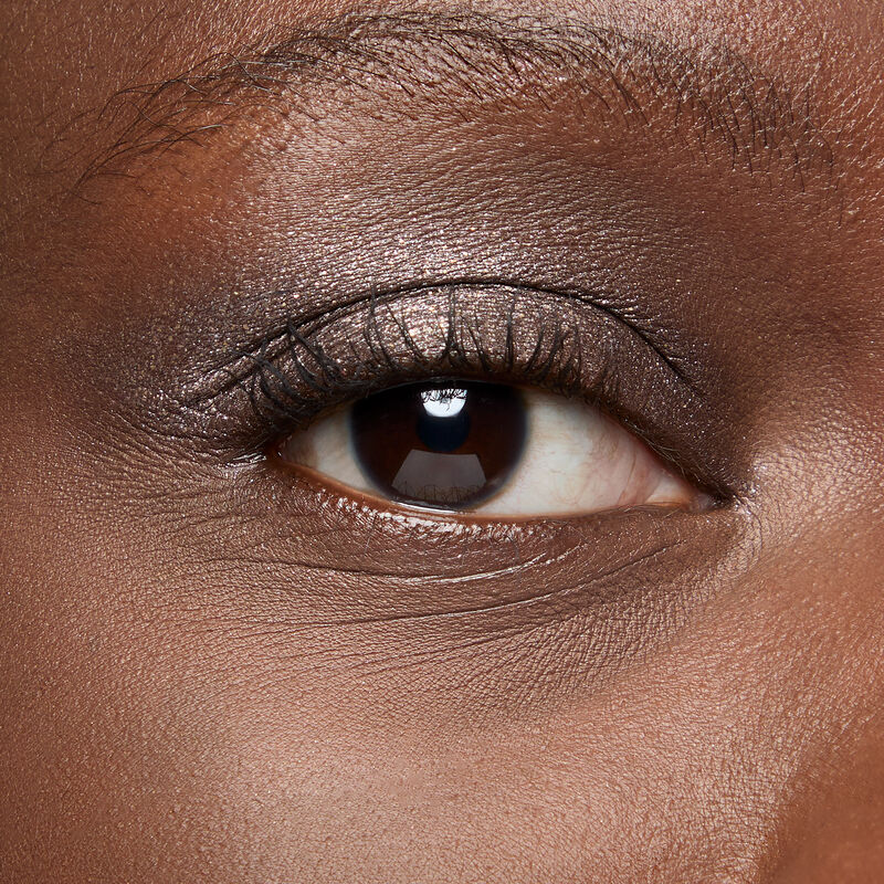 A model with a deep skin tone and brown eyes wears shade Midnight Galaxy