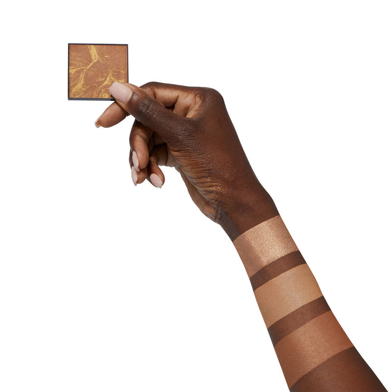 Hand dunklere Hautfarbe h&auml;lt Bronzer. Farbmuster der Bronzer auf dem Arm. 