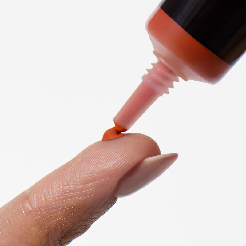 A close-up shot of Mary Kay&reg; Undereye Corrector&rsquo;s needle nose squeezing out a dot of product in shade deep peach on a finger