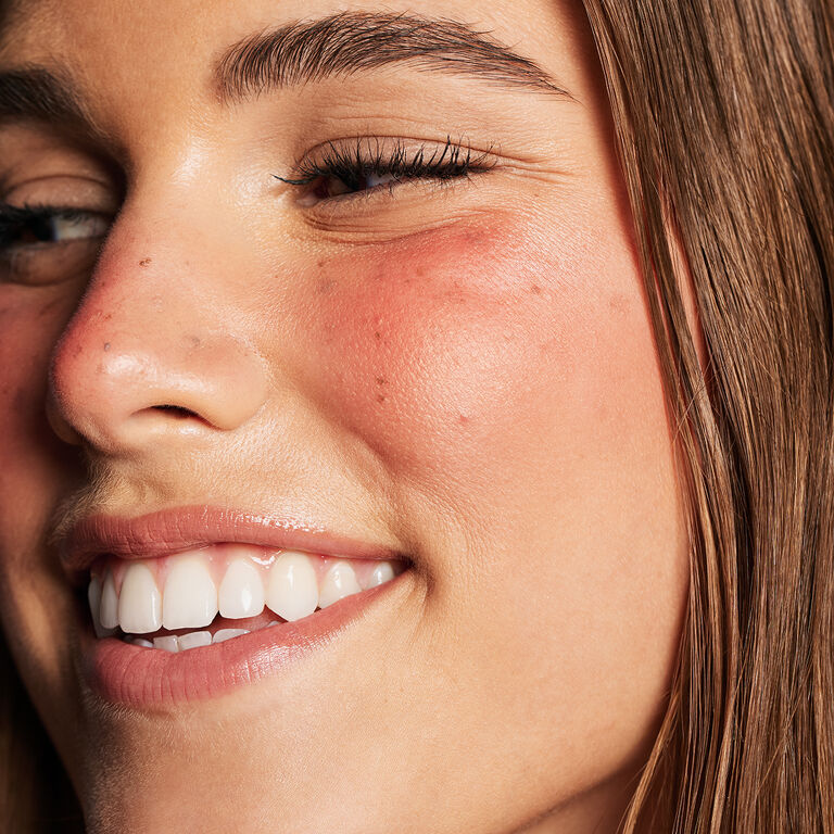 Eine lachende Frau, deren Gesicht mit dem "Strawberry Makeup" Trend geschminkt ist: Fake Freckles, glowy skin und sonnengek&uuml;sste Wangen