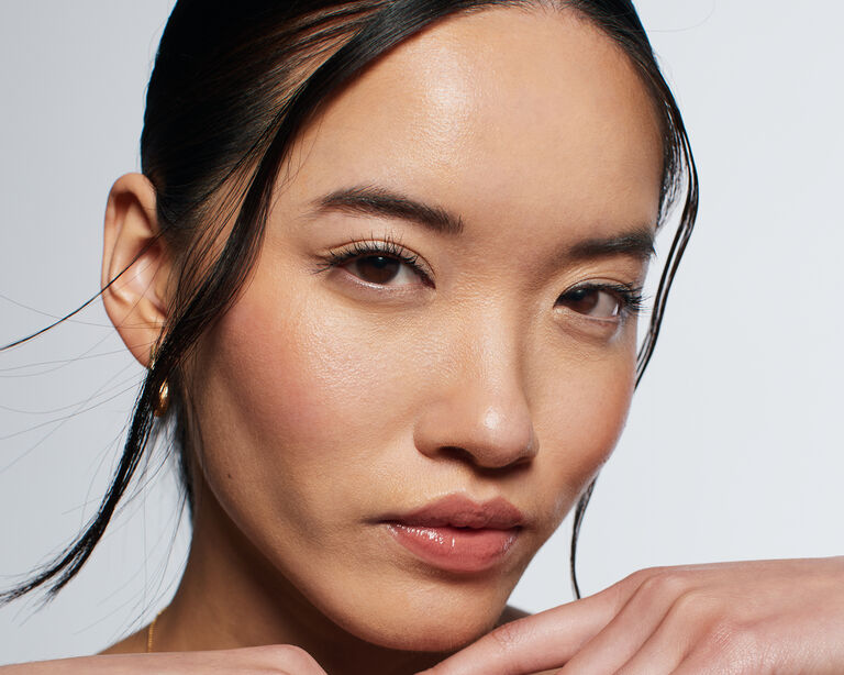 Eine Frau, die den Make-up Look Underpainting tr&auml;gt, in die Kamera blickt und ihre H&auml;nde unterhalb des Kopfes h&auml;lt