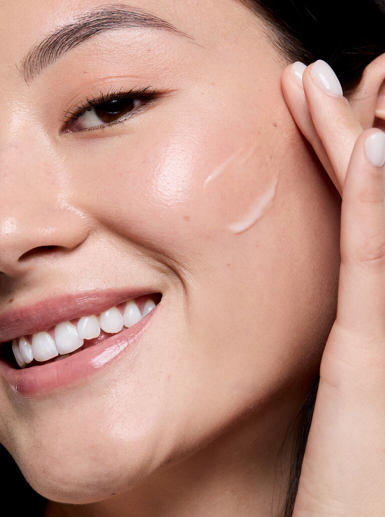 Nahaufnahme eines Gesichts mit strahlender Haut, w&auml;hrend eine Frau das Mary Kay Retinol Serum mit den Fingern auf die Wange auftr&auml;gt.