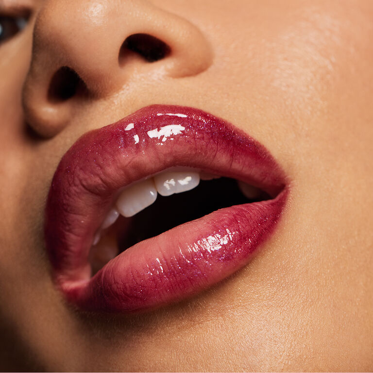 Eine Frau mit lockigem Haar, die den Make-up Trend Glass Lips tr&auml;gt: Ihre Lippen gl&auml;nzen und sehen gepflegt aus