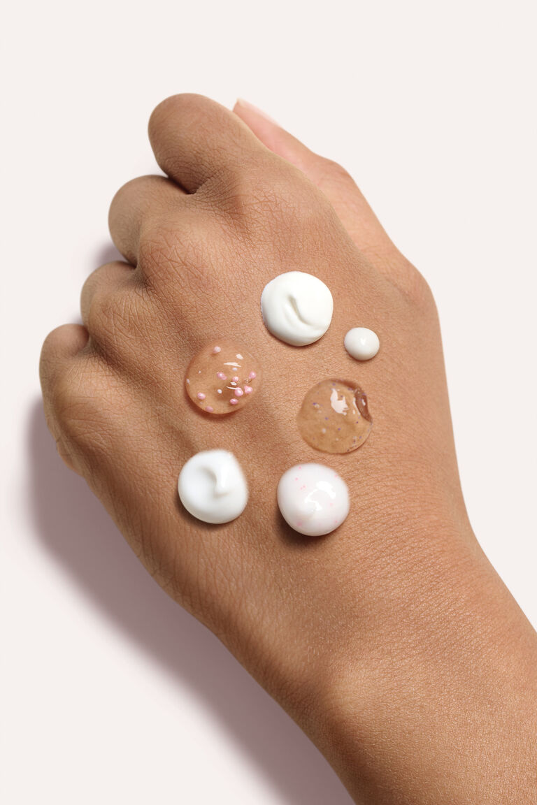Eine Hand, auf der Produktkleckse der sechs Produkte aus dem TimeWise Ultimate Wunder-Set von Mary Kay zu sehen sind