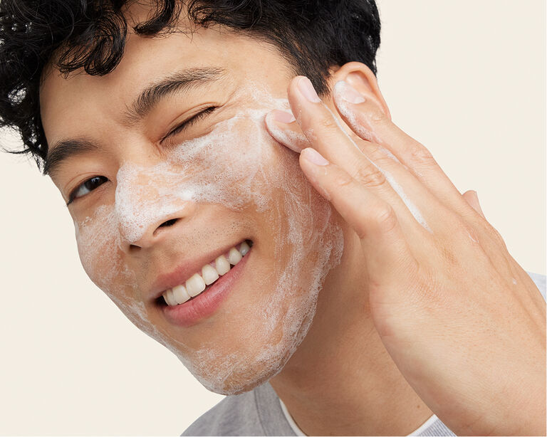 Nahaufnahme eines Mannes, der ein Auge geschlossen hat und mit einer Hand den sch&auml;umenden MK Men Daily Facial Wash (Cleanser) im Gesicht verteilt