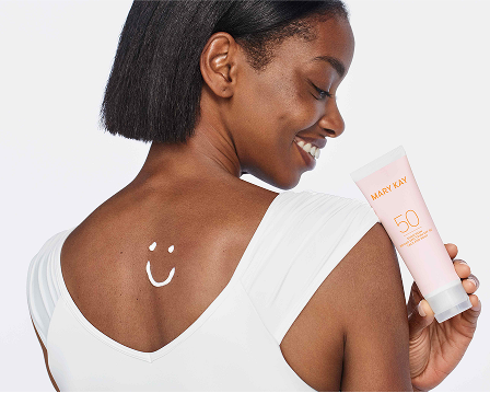 Eine l&auml;chelnde Frau in einem wei&szlig;en Top cremt sich eine Schulter mit dem Mary Kay After Sun Replenishing Gel ein