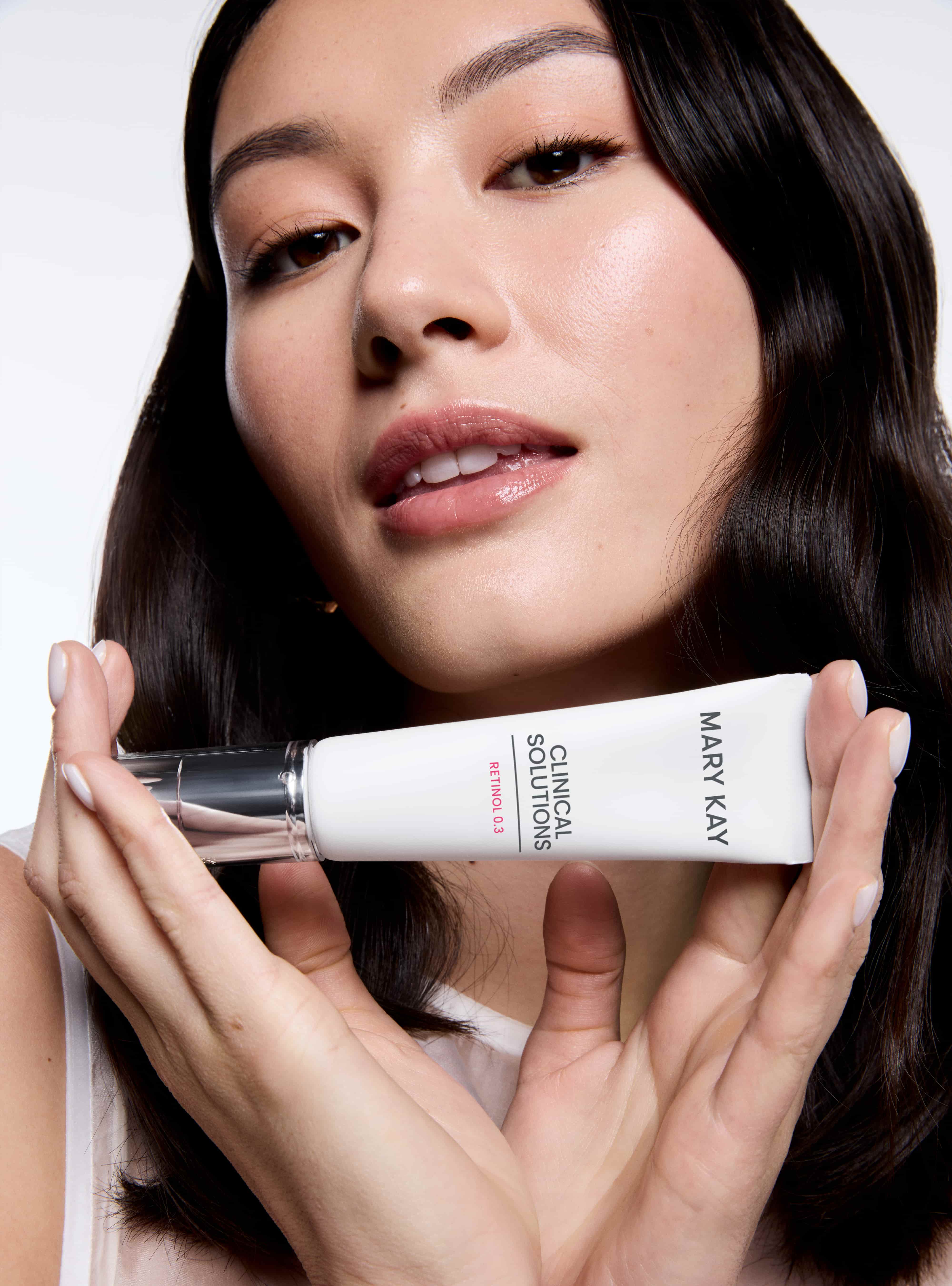 Eine Frau mit strahlender Haut hält in beiden Händen das Clinical Solutions Retinol 0,3 Serum von Mary Kay