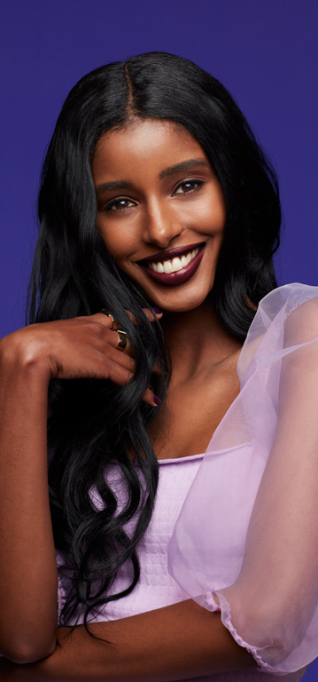 Eine Frau mit dunklem Haar und dunklem Hauttyp tr&auml;gt den Mary Kay Supreme Hydrating Lipstick in Black Cherry und l&auml;chelt in die Kamera
