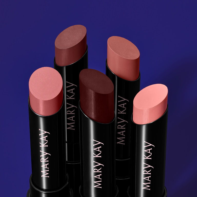 Verschiedene rote, pinke und nudefarbene Supreme Hydrating Lipsticks von Mary Kay vor einem blauen Hintergrund