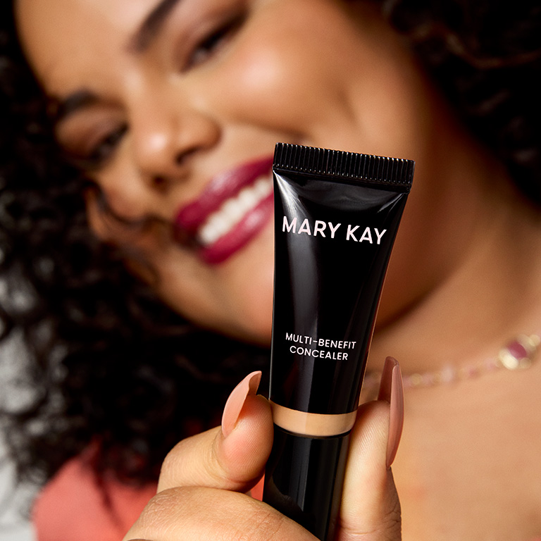 Nahaufnahme des Mary Kay Multi-Benefit Concealer in einem mittleren Farbton, den eine Frau vor ihr Gesicht h&auml;lt (die Frau ist im Hintergrund verschwommen zu sehen)