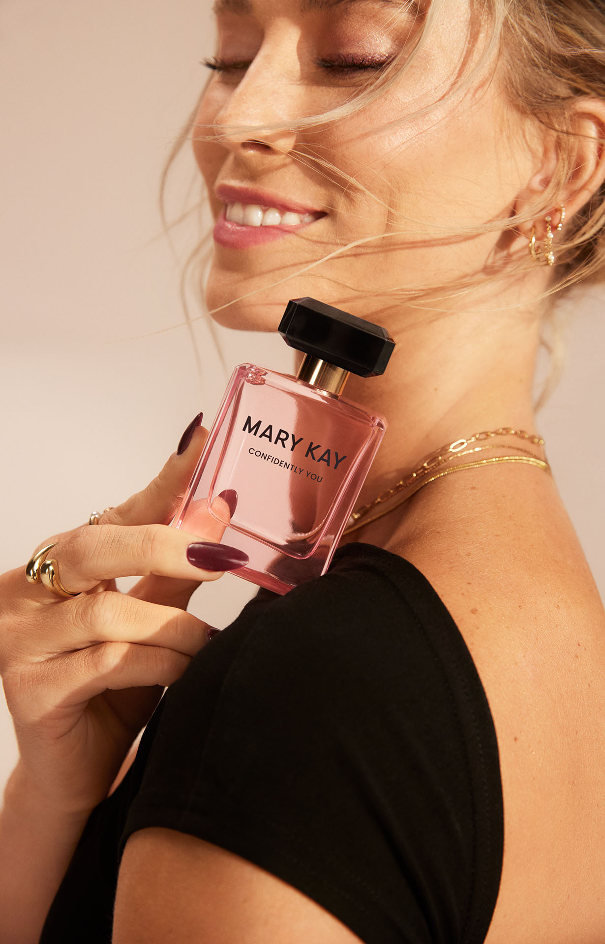 Eine Frau mit geschlossenen Augen hält in einer Hand das Mary Kay Confidently You Parfum (rosa Flakon mit schwarzem Deckel)