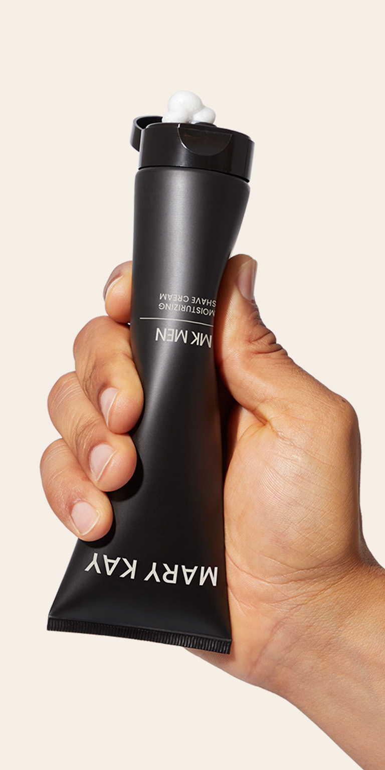 Nahaufnahme der Tube der MK Men Moisturizing Shave Cream, aus der eine Hand etwas wei&szlig;es Produkt herausdr&uuml;ckt