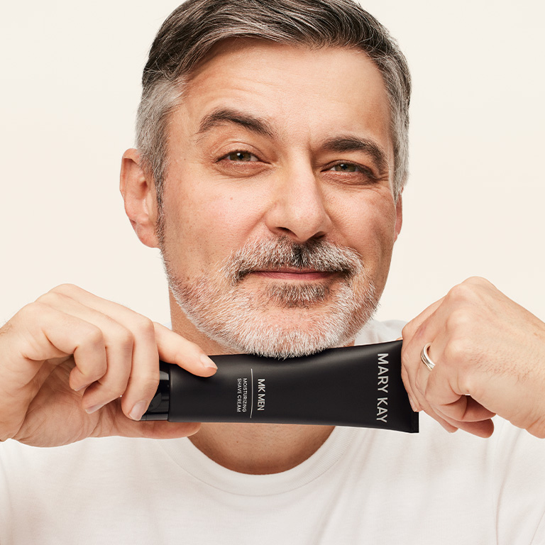 Ein Mann mit Kurzhaarschnitt und kurzem Bart h&auml;lt die MK Men Moisturizing Shave Cream von Mary Kay mit beiden H&auml;nden unterhalb seines Kinns