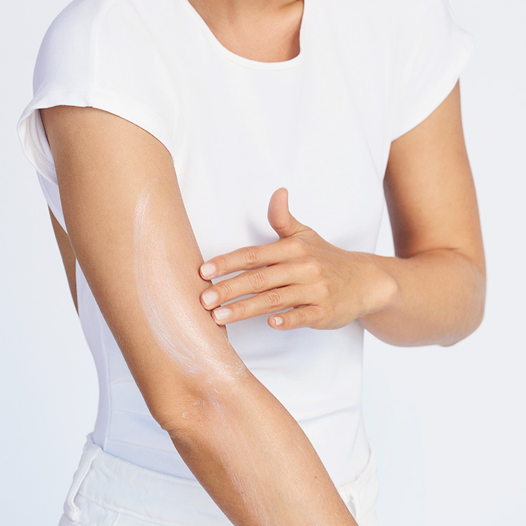 Eine ganz in wei&szlig; gekleidete, blonde Frau tr&auml;gt die 50+ Sonnencreme von Mary Kay auf ihrem Arm auf