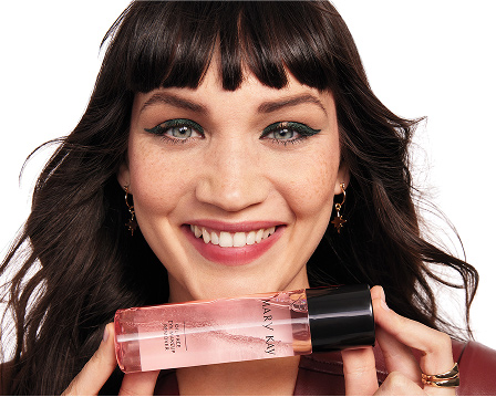 Eine l&auml;chelnde Frau mit geschminktem Gesicht (Eyeliner und Mascara) h&auml;lt den Oil-Free Eye Makeup Remover von Mary Kay in beiden H&auml;nden und sch&uuml;ttelt ihn