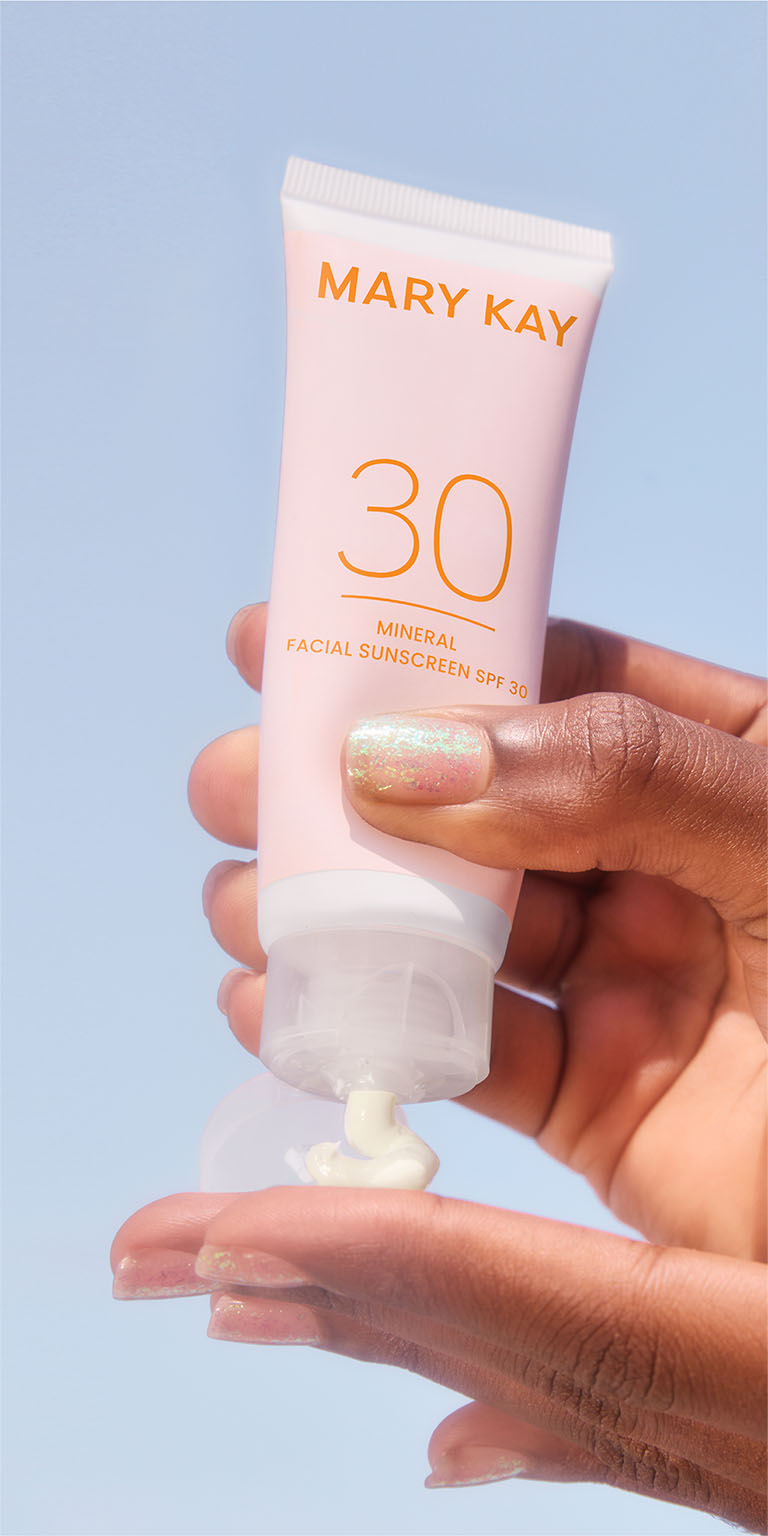 Nahaufnahme der H&auml;nde einer Frau vor einem himmelblauen Hintergrund: Die Frau dr&uuml;ckt mit einer Hand eine kleine Menge der Mineral Facial Sunscreen LSF 30 heraus und gibt sie auf ihre andere Hand