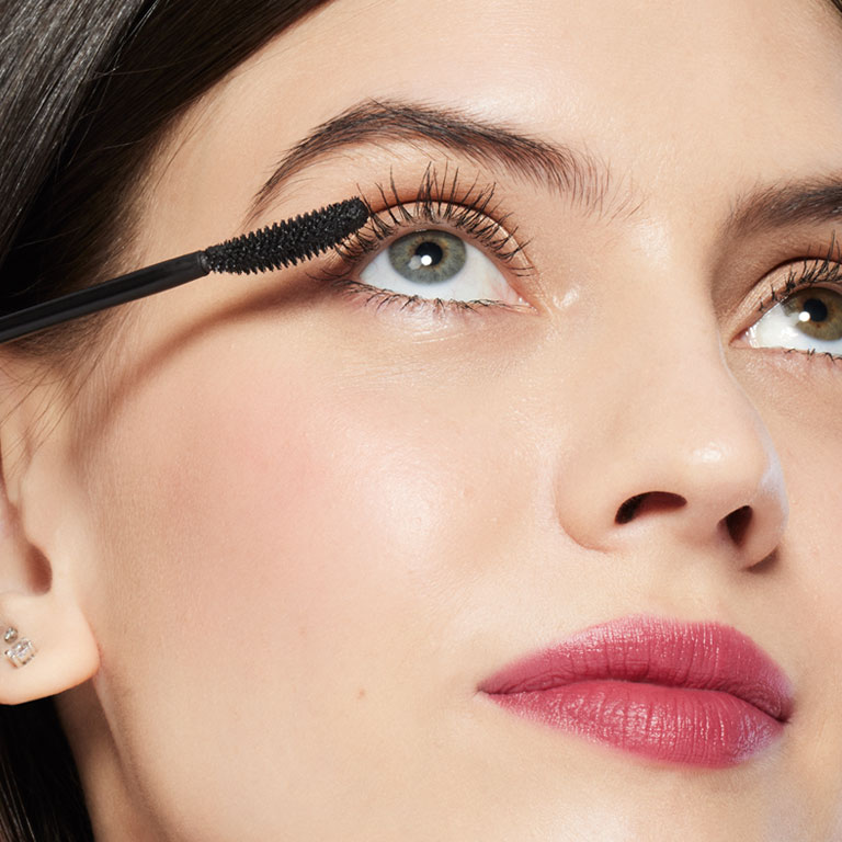 Blonde model holding Mary Kay Great Heights Mascara applicator up to her eye