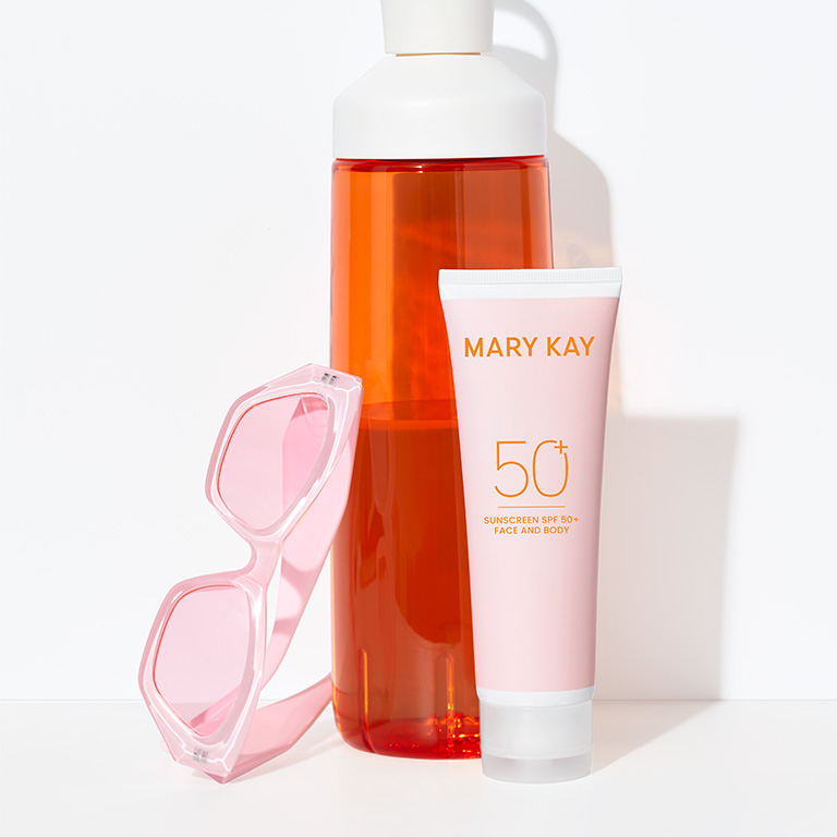 Neben einer Sonnenbrille in Rosa und einer Trinkflasche in Orange steht die rosa Tube von Mary Kay auf einem wei&szlig;en Untergrund: Sunscreen SPF 50+ Face and Body