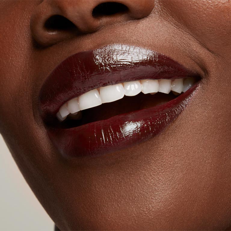 Nahaufnahme des Gesichts einer Frau mit dunklem Hauttyp, die den Mary Kay Supreme Hydrating Lipstick in einem dunklen Ton (Black Cherry) tr&auml;gt und l&auml;chelt